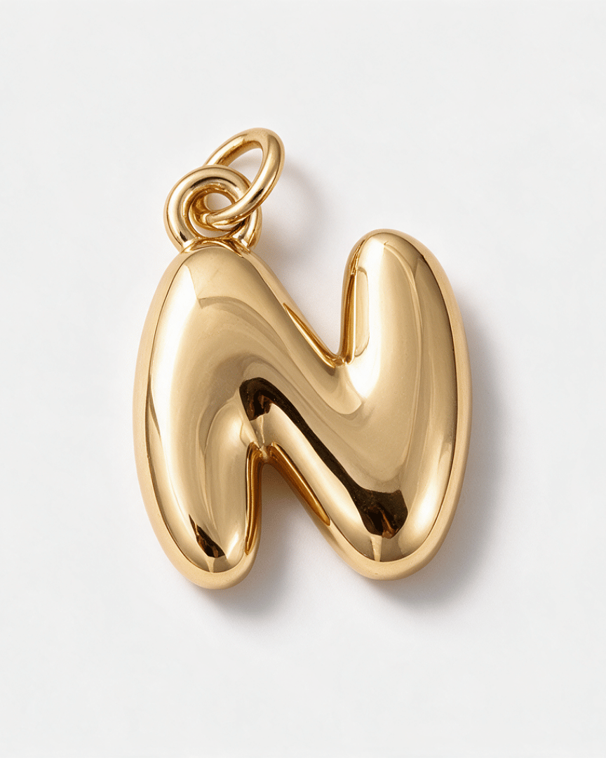 A polished gold initial pendant shaped like the letter 'M', featuring a smooth, reflective surface and a top loop for a chain, shown on a clean white background.