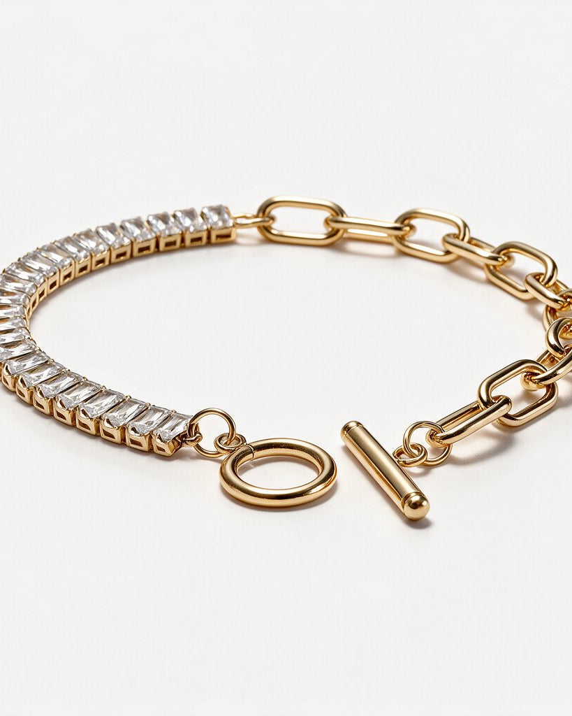 collection-image A gold-toned bracelet featuring a row of clear rectangular stones along one side, a curb chain link section, and a toggle clasp, photographed on a clean white background.